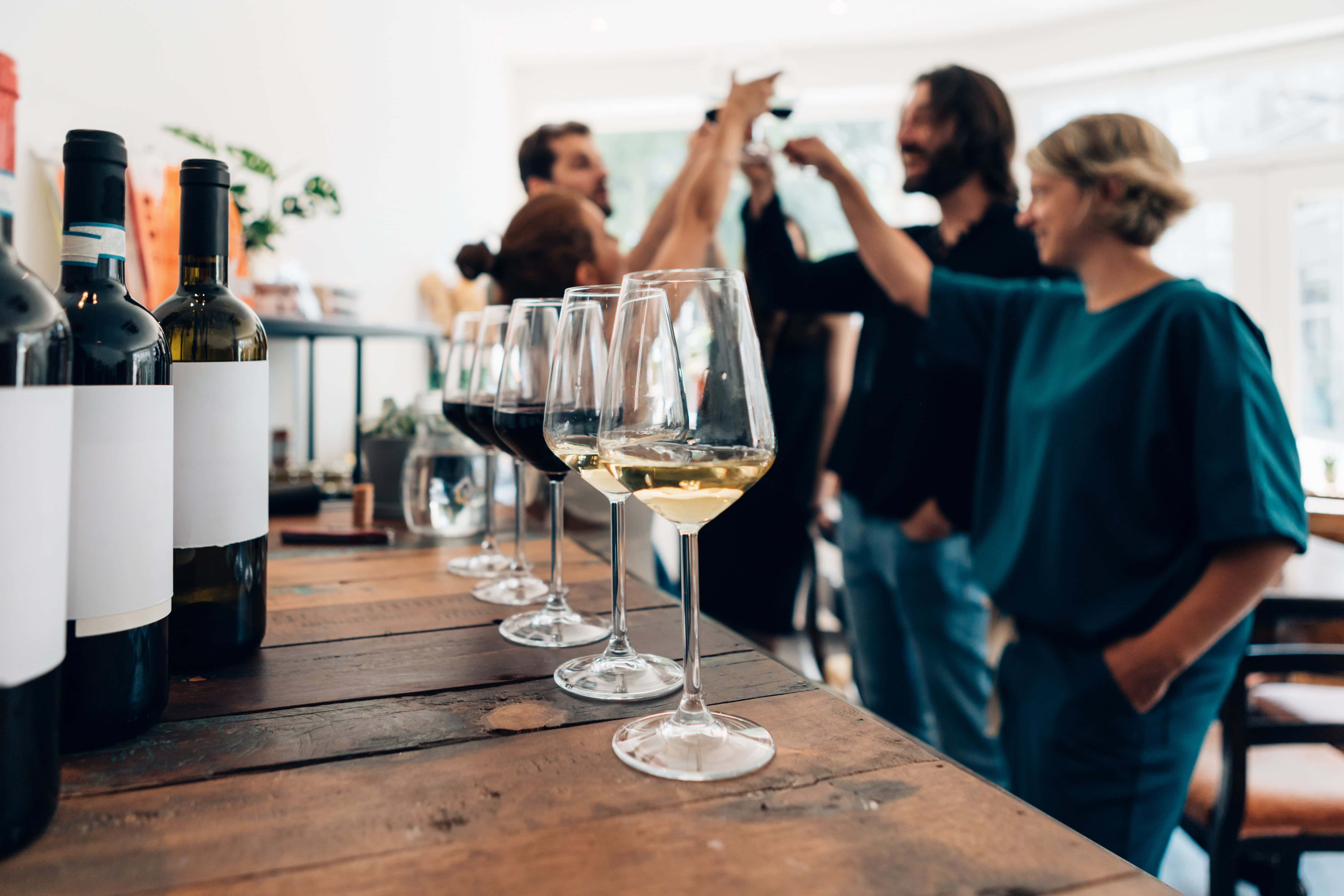 Wine tasting event with glasses of red and white wine on a rustic wooden table as a group of friends toasts in the background.