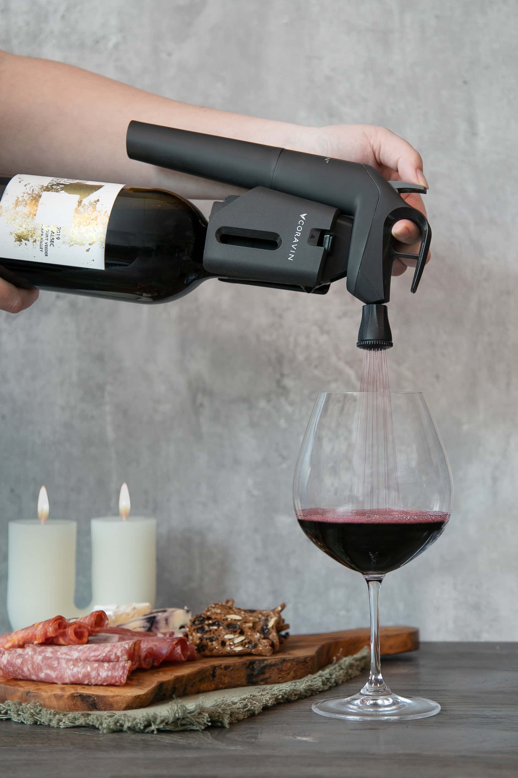 Pouring red wine using Coravin Timeless Three+ wine preservation system, with a charcuterie board and candles in the background.