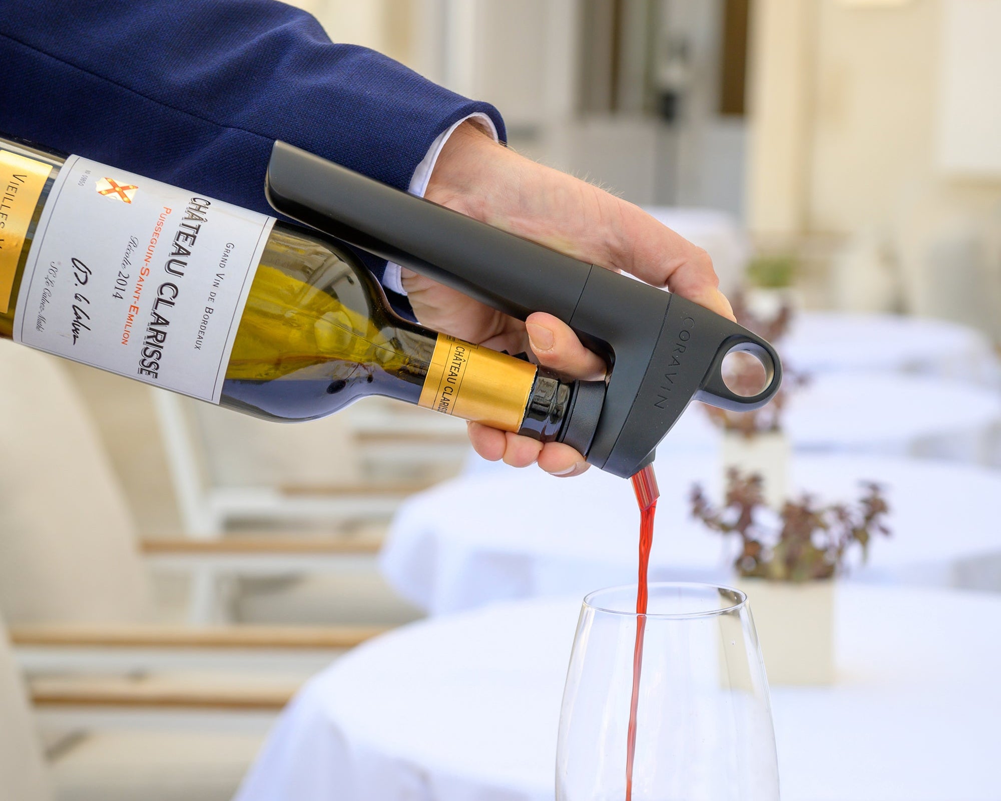 Person pouring red wine from a bottle into a glass on a table with a blurred background