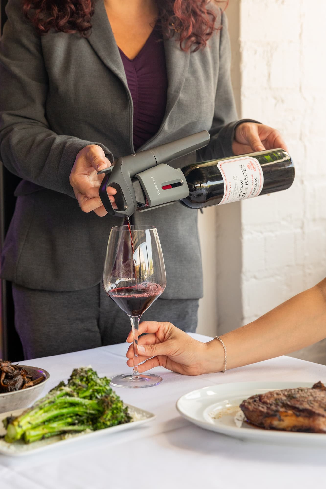 a person uses a Coravin wine by-the-glass system to pour red wine into a glass, a fine dining setting enhanced by wine-by-the-glass technology