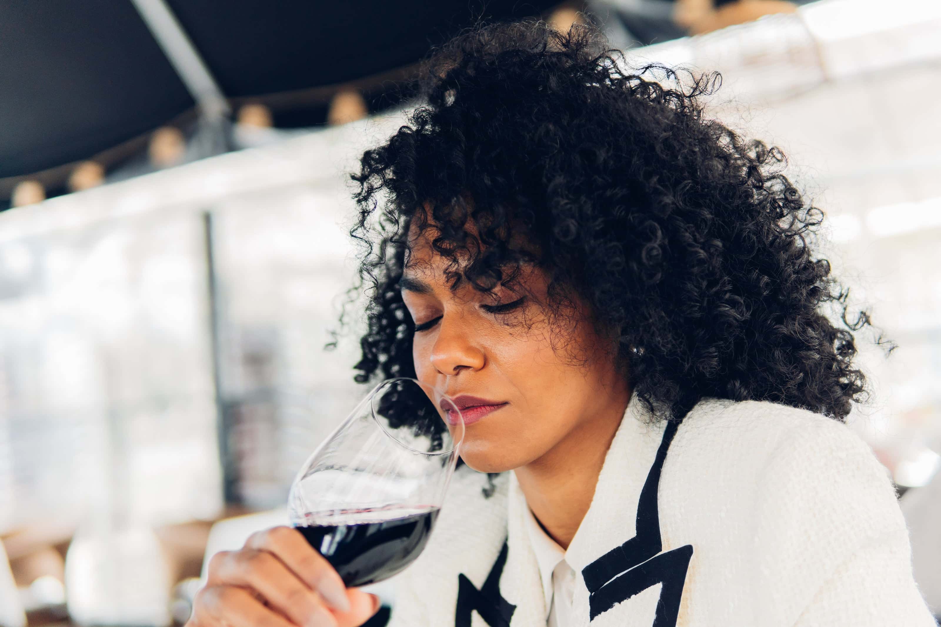 Woman with curly hair enjoying the aroma of a glass of red wine during a wine tasting experience.