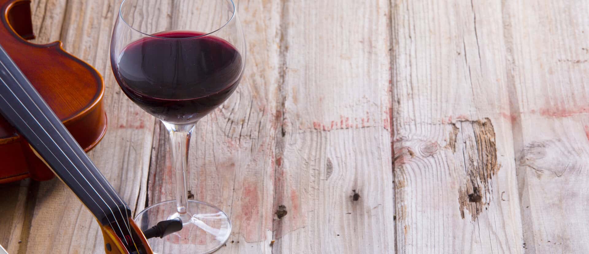 Glass of red wine and a violin resting on a rustic wooden table, symbolizing the harmonious connection between music and winemaking.