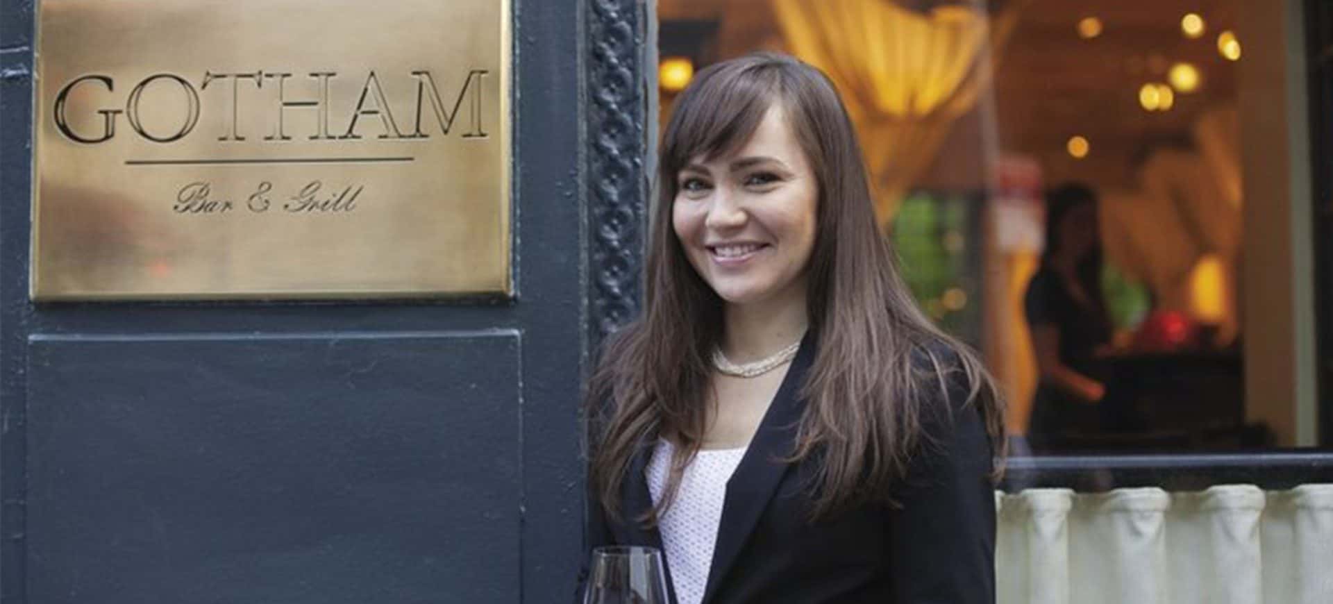 Heidi Turzyn, Beverage Director at Gotham Bar and Grill, smiling outside the restaurant while holding a glass of wine