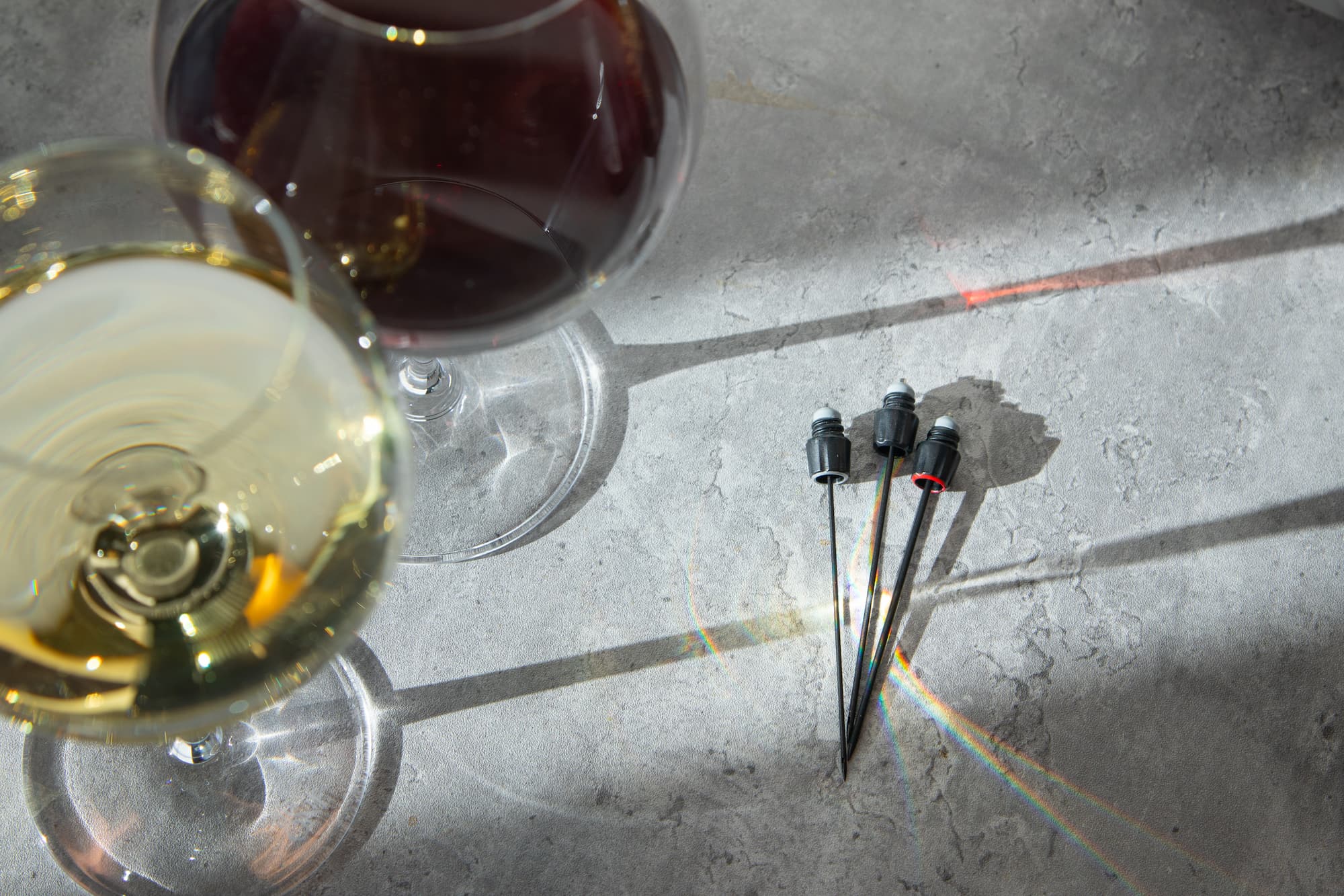 three coravin wine saver needles on slate table with red and white wine