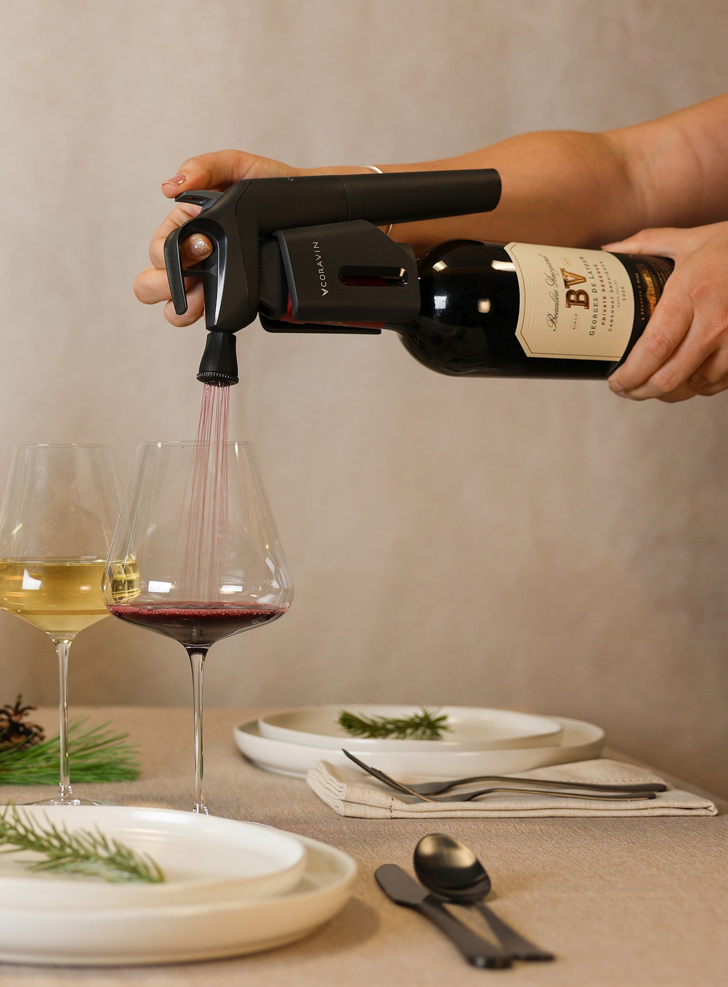 Person pouring wine into a glass on a decorated table with bottles and plates.