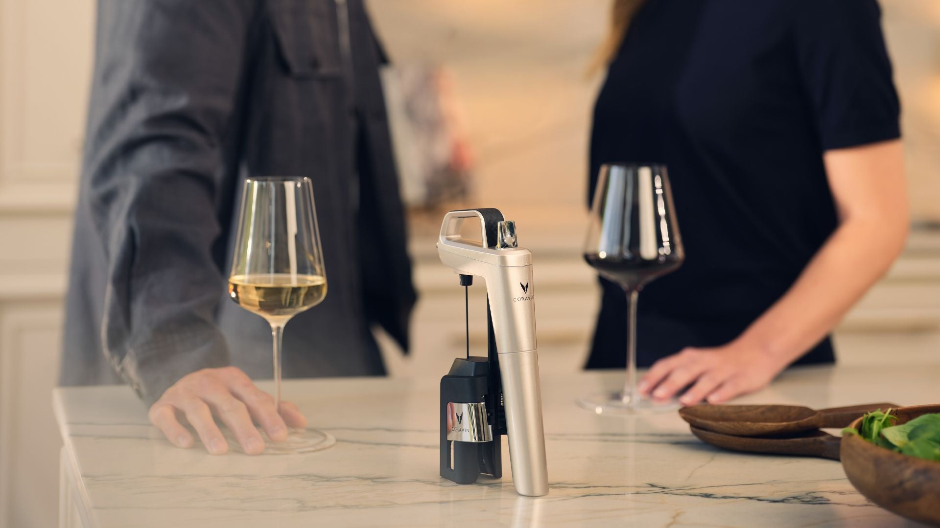 Two people with wine glasses and a Coravin Timeless Six Silver on a table.
