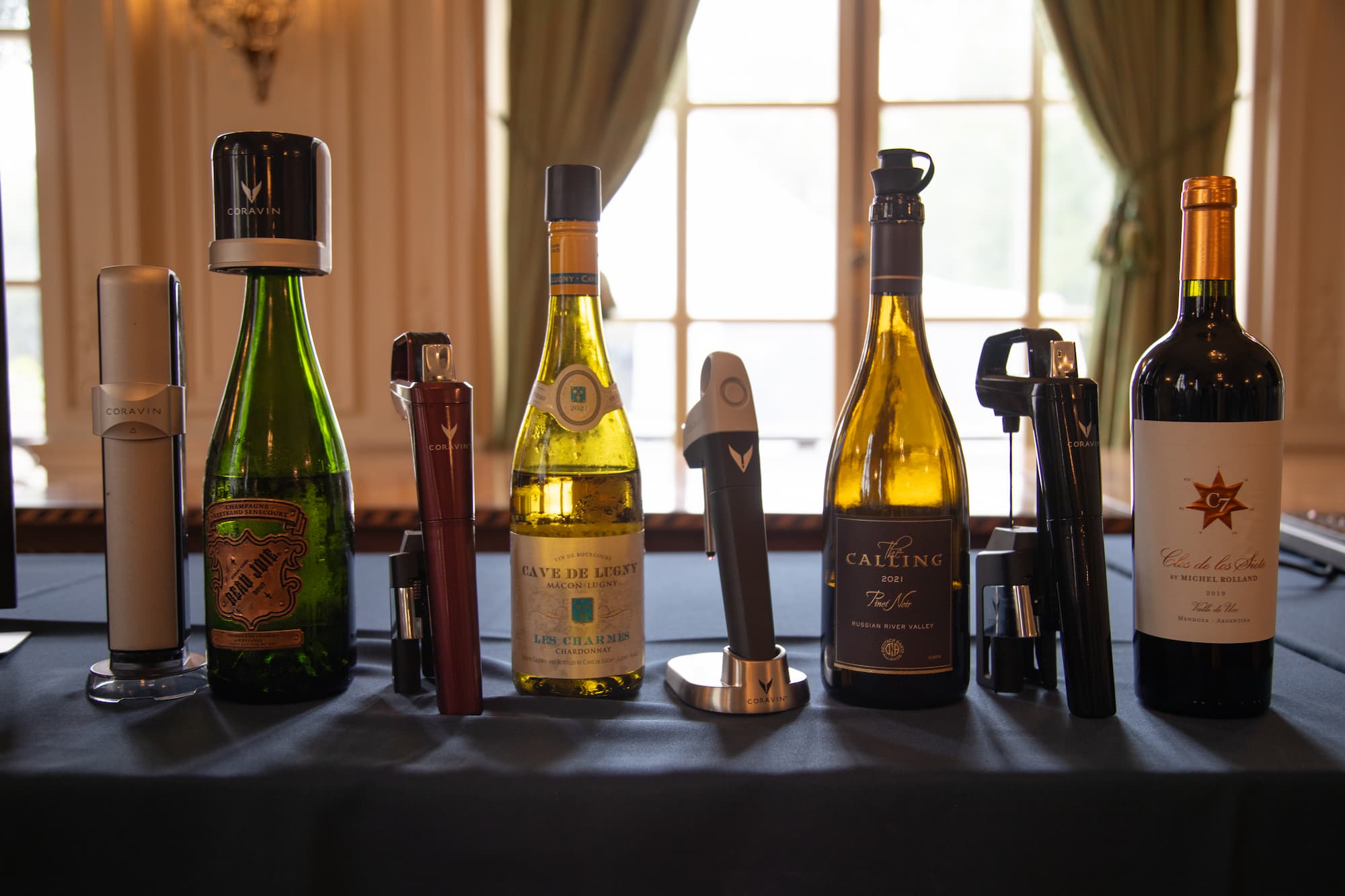 Six wine bottles displayed on a table, each paired with a different style of Coravin systems