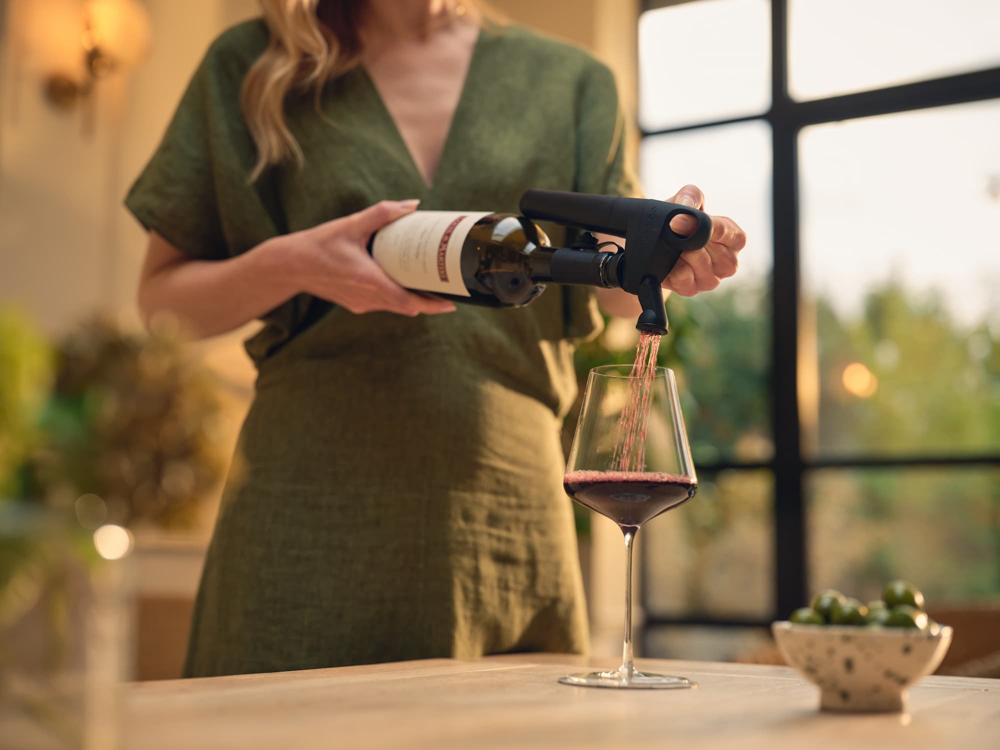 Person using a Coravin wine Pivot system to pour red wine into a glass, suggesting a sophisticated wine-tasting moment