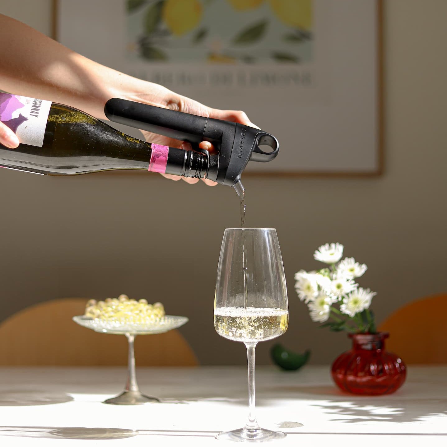 Person pouring white wine through a sleek Coravin Pivot+ aerator into a glass, capturing a moment of wine enjoyment