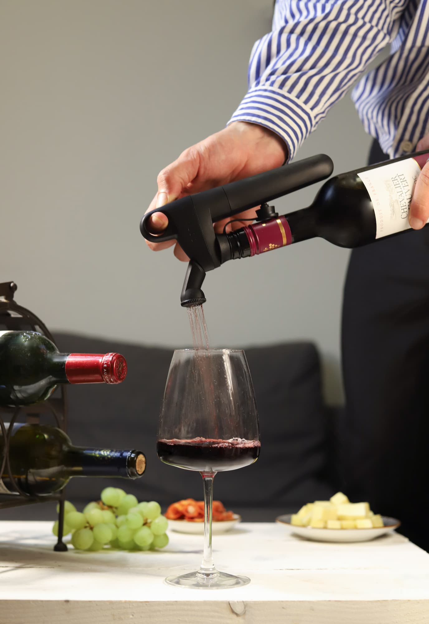 Person using a Coravin Pivot wine-by-the-glass system to pour red wine into a glass on a white table