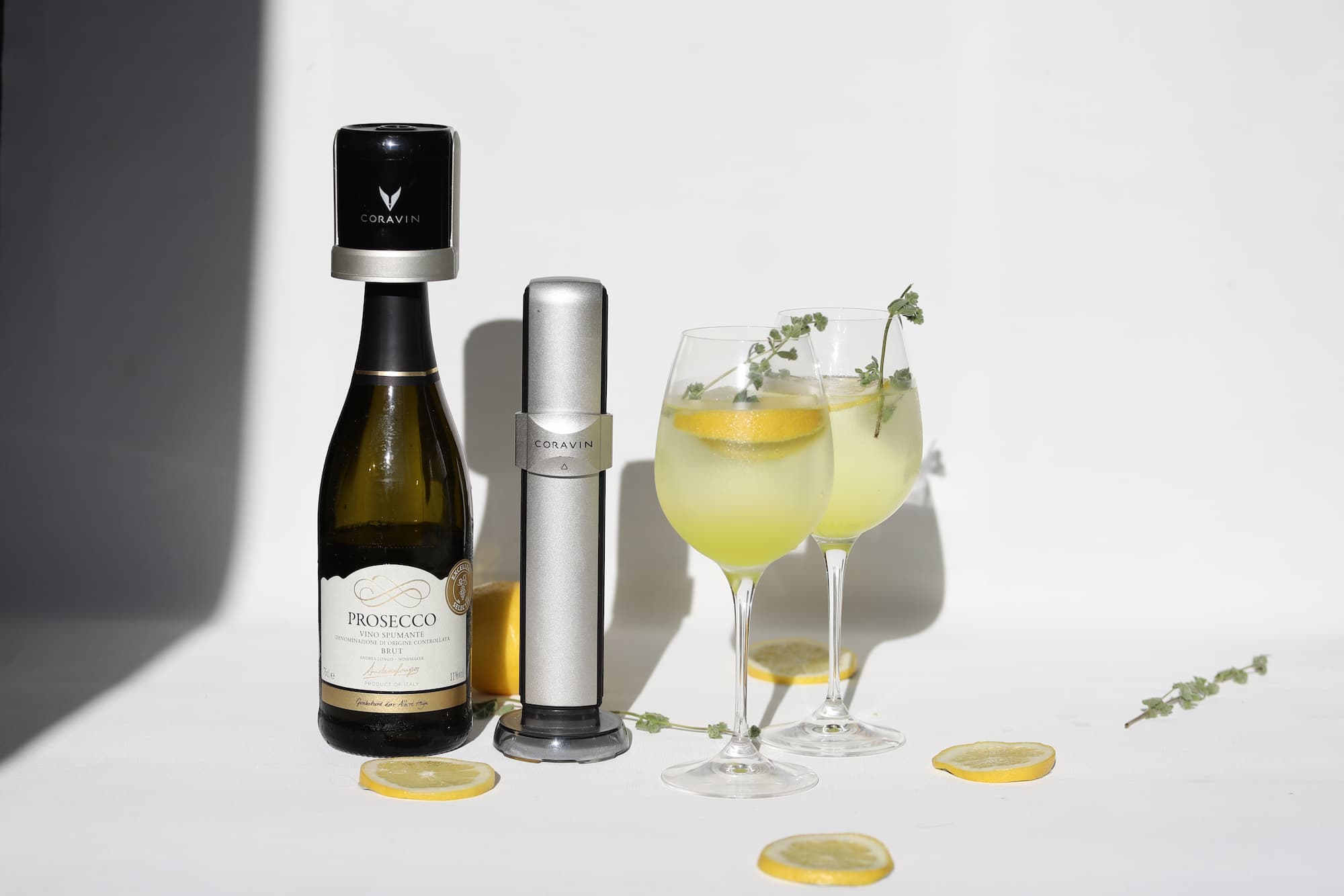 A Prosecco bottle using a Coravin Sparkling Stopper and two wine glasses with lemon slices decoration
