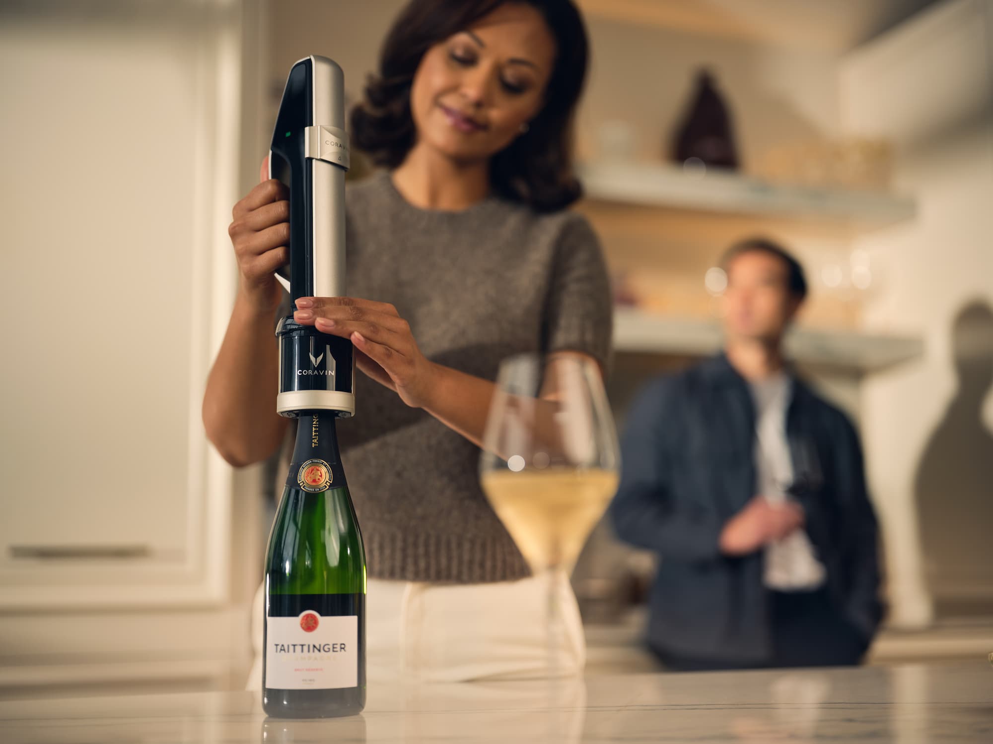 Person using a Coravin wine sparkling system to pour champagne from a  bottle into a glass on a kitchen counter, modern, social setting