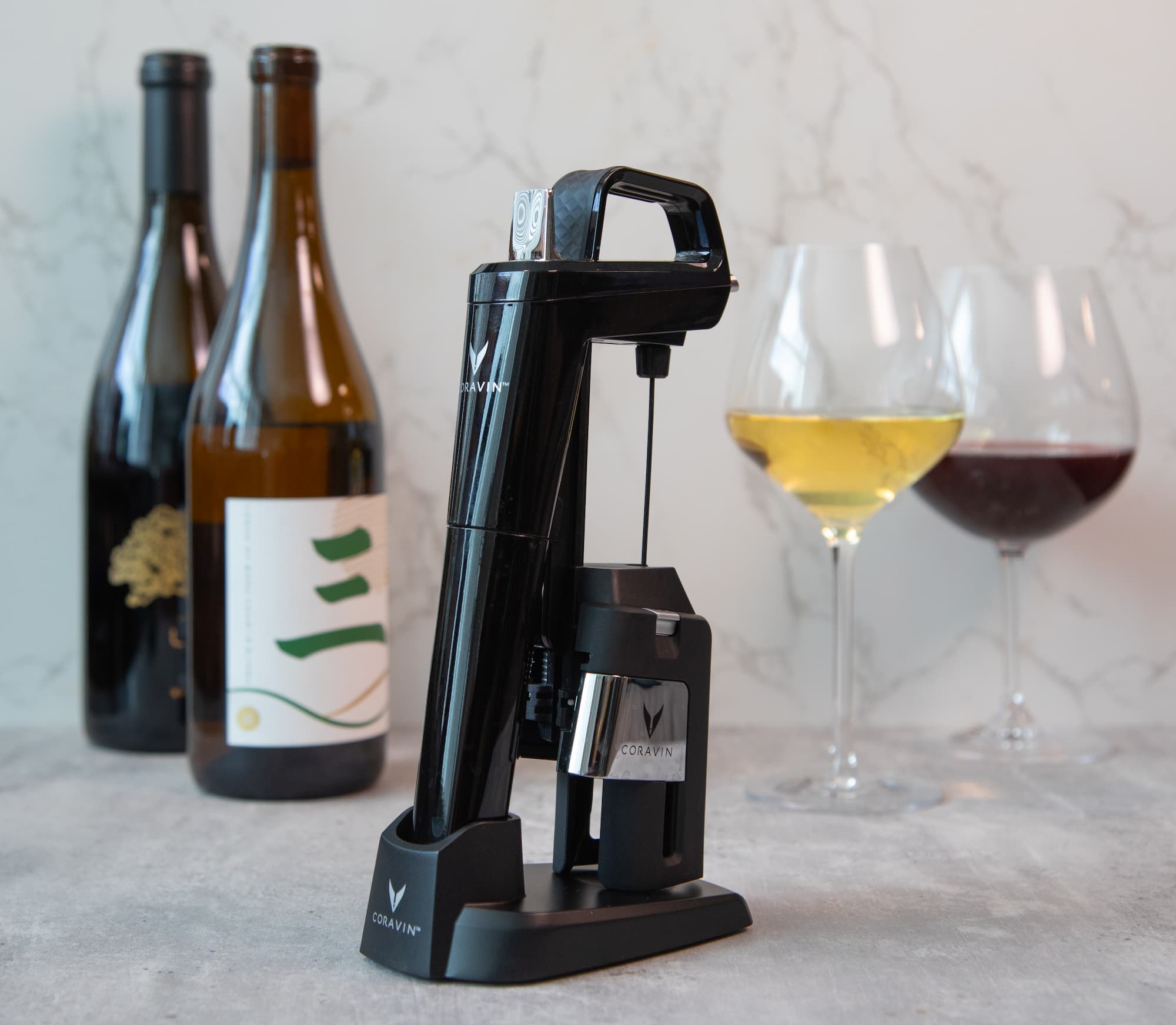 a sleek black Coravin wine-by-the-glass-system displayed on a countertop alongside two wine bottles and glasses