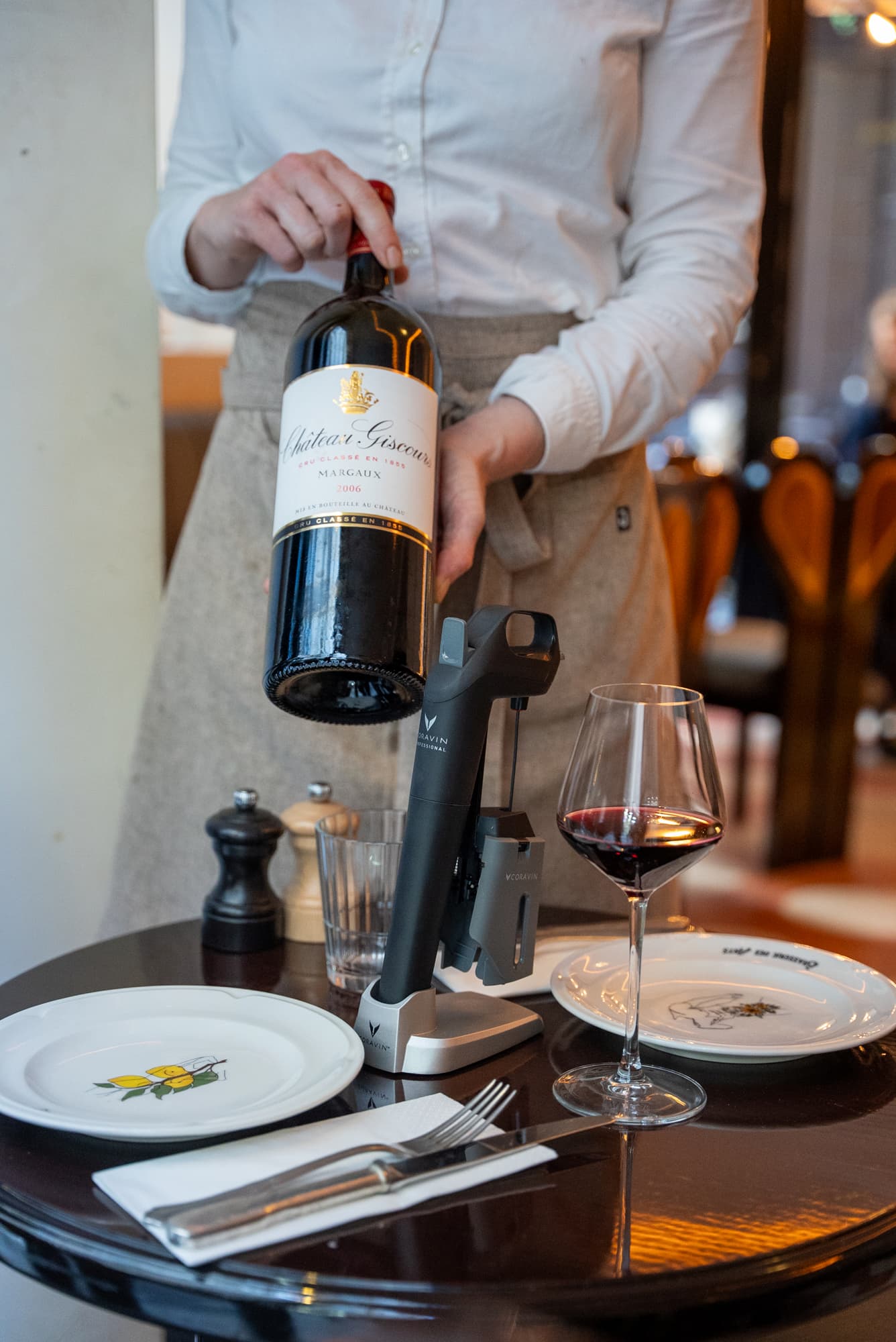 Person serving a premium wine bottle using Coravin wine-by-the-glass system, capturing refined wine service