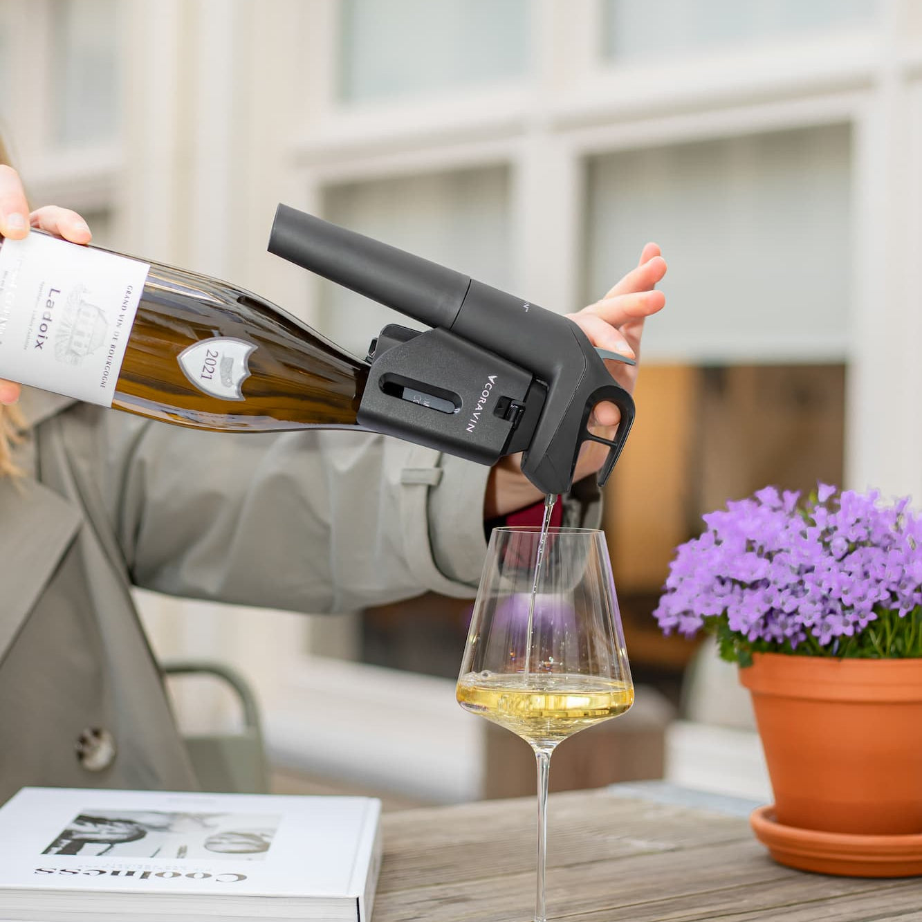 a person outdoors pours white wine using a Coravin wine-by-the-glass preservation system into a glass
