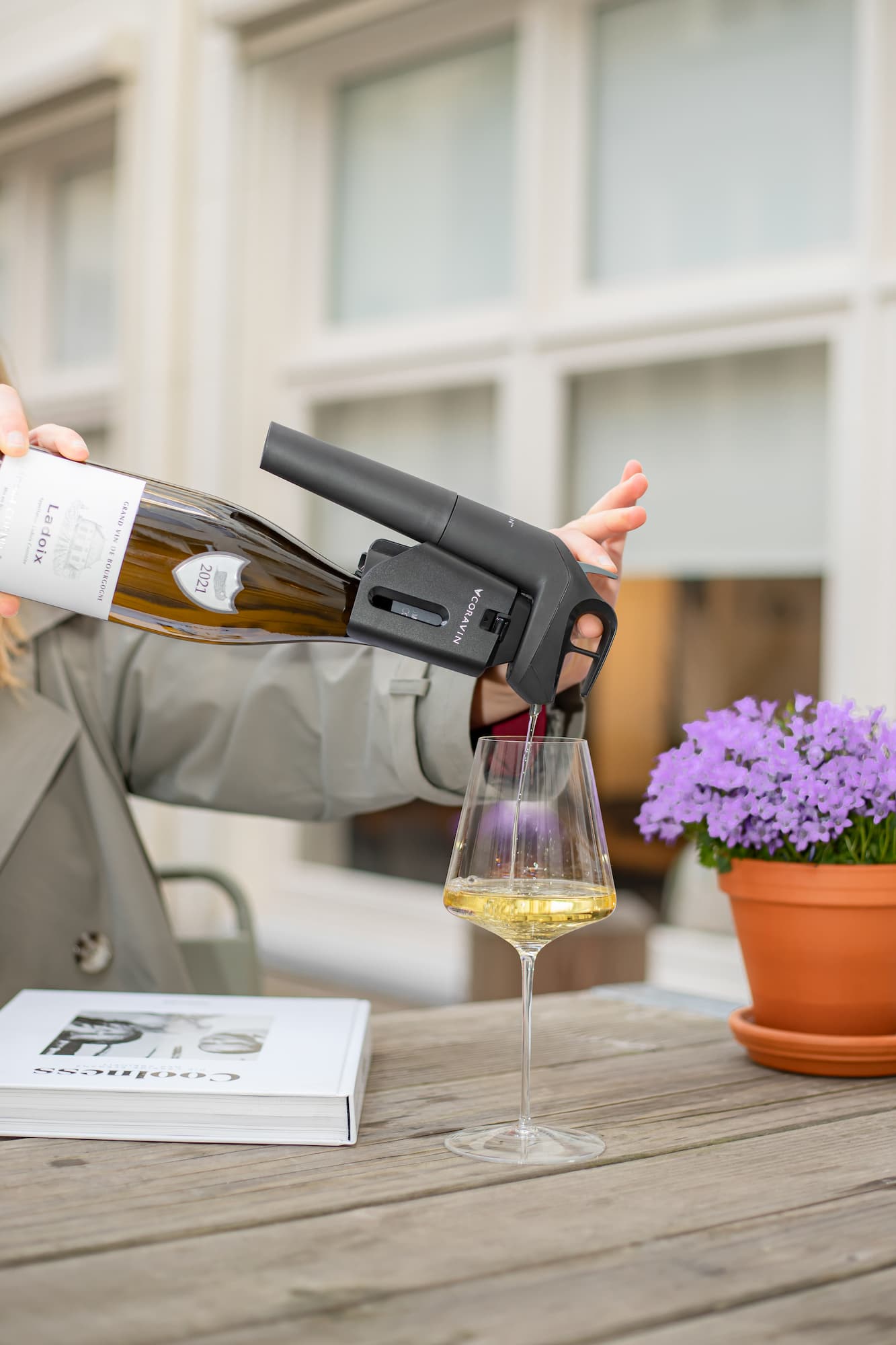 a person outdoors pours white wine using a Coravin wine-by-the-glass preservation system into a glass