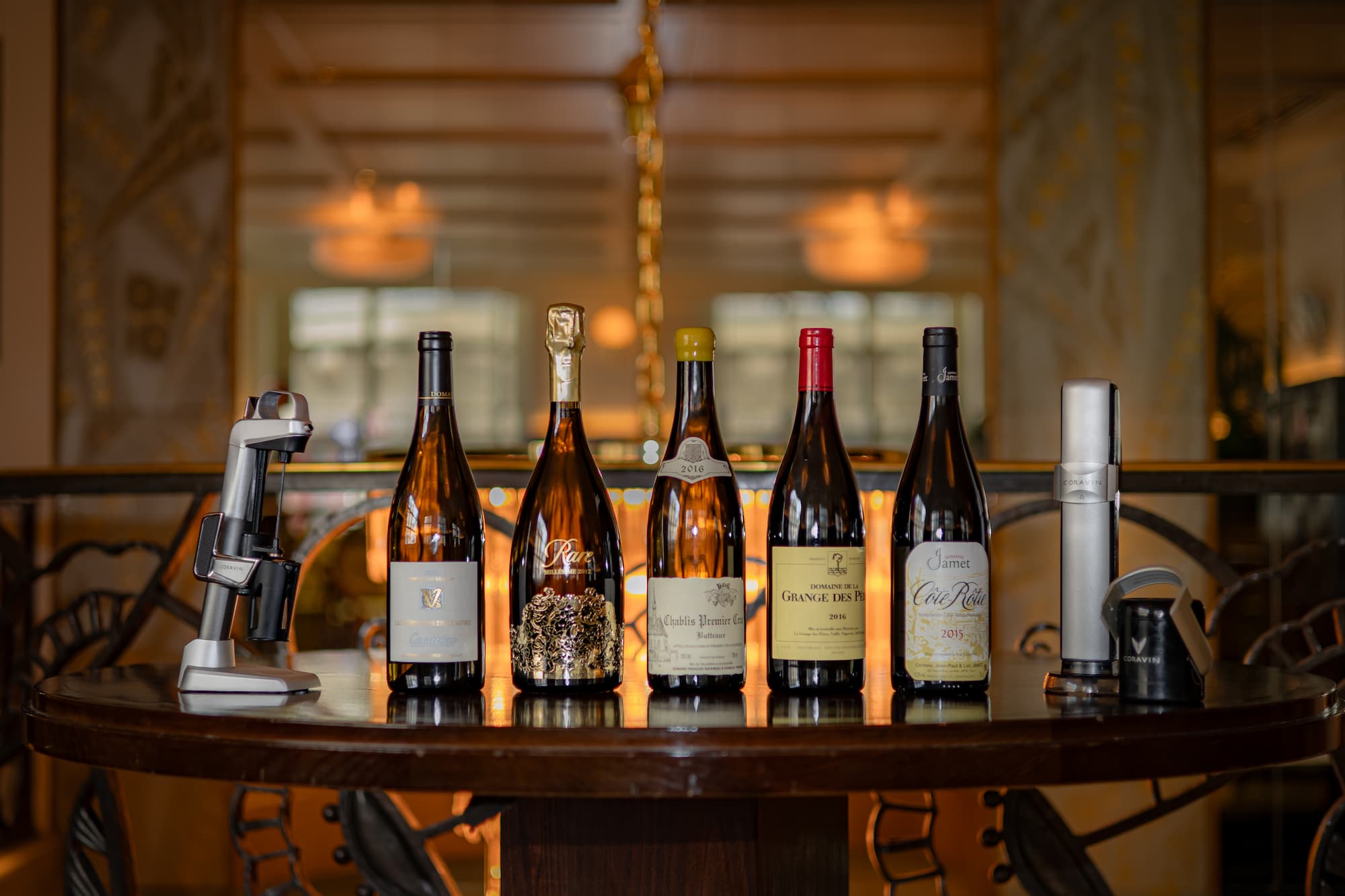 Five wine bottles accompanied by Coravin wine-by-the-glass devices, showcasing a luxurious tasting experience 